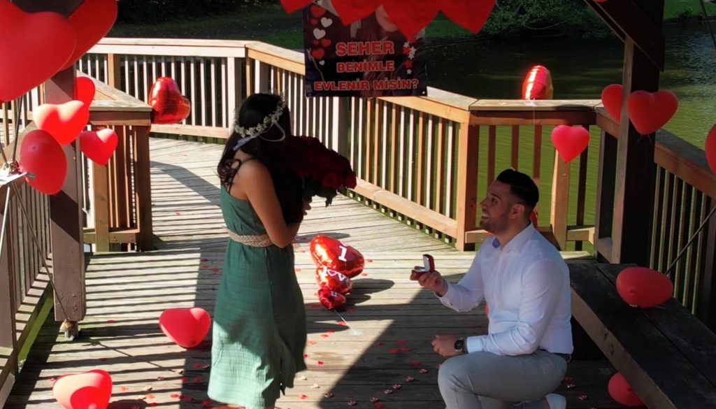 Ein Hochzeitsantrag auf einem Steg mit roten Luftballons